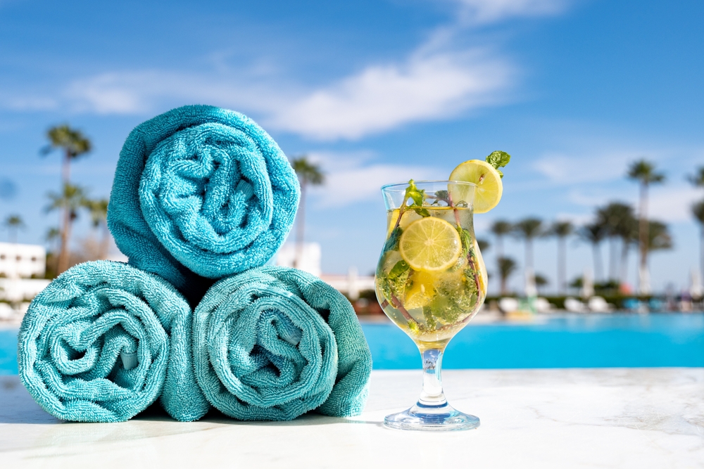 Three towels, rolled, sit next to a drink on a pool's edge: things to buy from Amazon for an all-inclusive resort help prepare for relaxation time to feature these items!>
