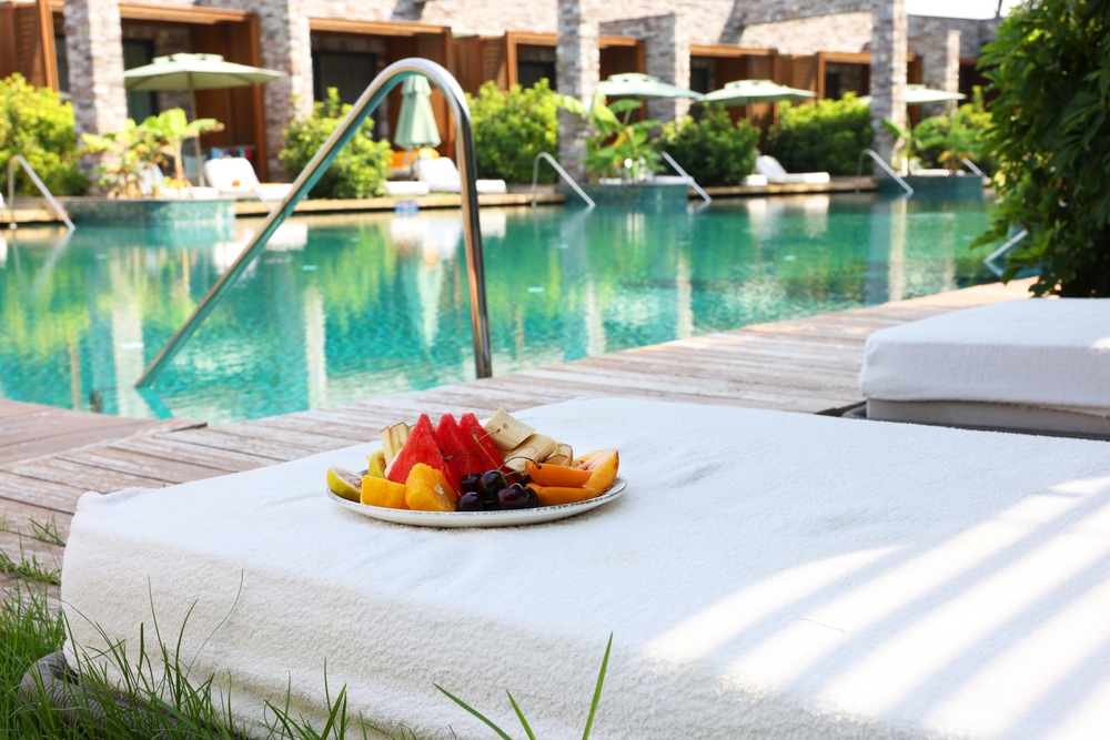 A fruit plate sits on a white cotton pool-bed by the pool itself, ready for guests.