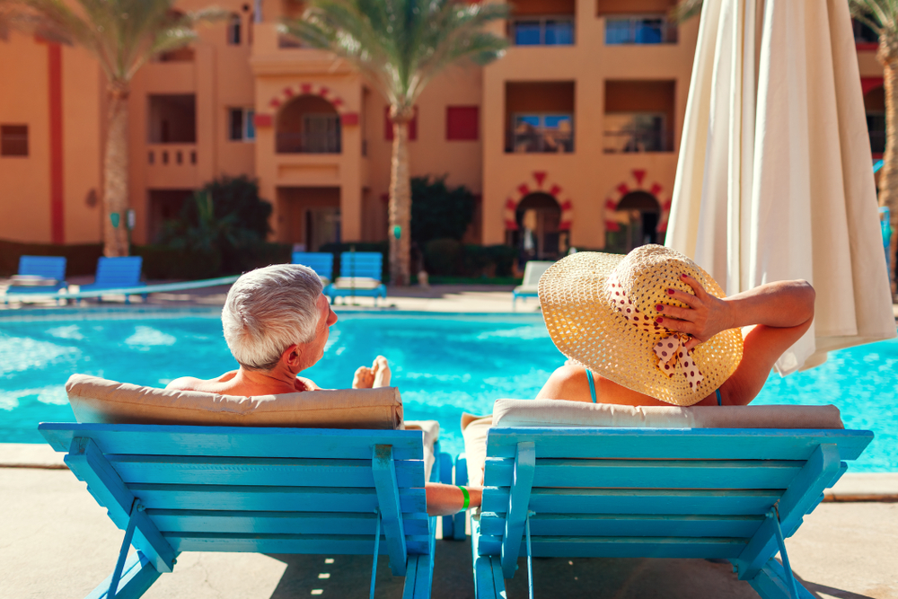 A couple sits on blue sun chairs, feet up, umbrellas by their side as they enjoy their time because they knew what things to buy from Amazon for an all-inclusive resort .