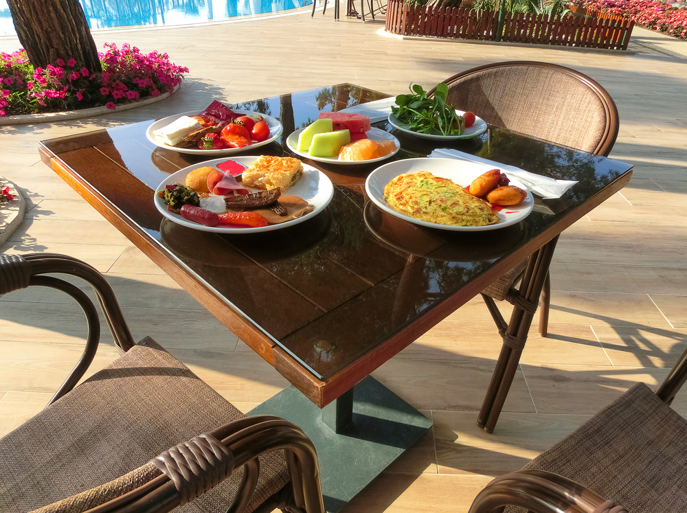 A photo of a private breakfast shows omelets, bacon, eggs , fruit, and more at wicker tables at an all-inclusive.