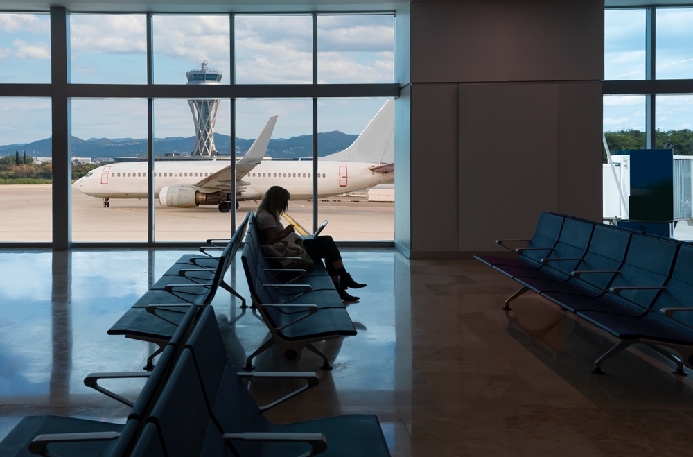 A woman sits on her laptop in an empty airport, the plane behind her ready to load.