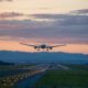 At dusk, a plane takes off, the runway light up, the skies pink, and mountains dark in the background: flying can be enjoyable when you know what things to buy from Amazon before flying.