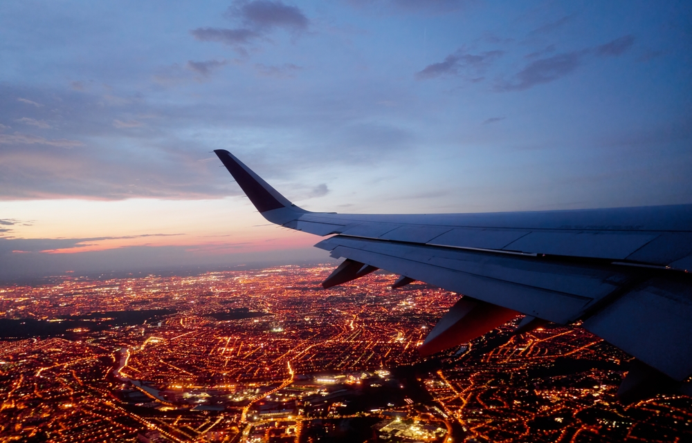 A plane's wing at night shows the city light's below, and the map of the areas as they glow, a view that can be enjoyable when people know what things to buy from Amazon before flying.