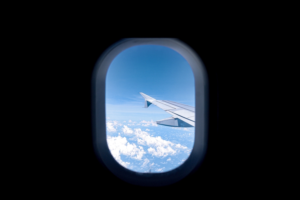 A dark shot of the plane reveals how dark the inside of the plane is, and how bright the window is as it looks out over the wing and blue skies and white clouds.