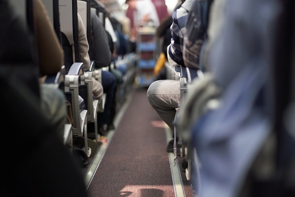 A shot down the aisle of the plane shows feet and legs and seats, all of which can be made comfortable if you know what things to buy from Amazon before flying: like a footrest!