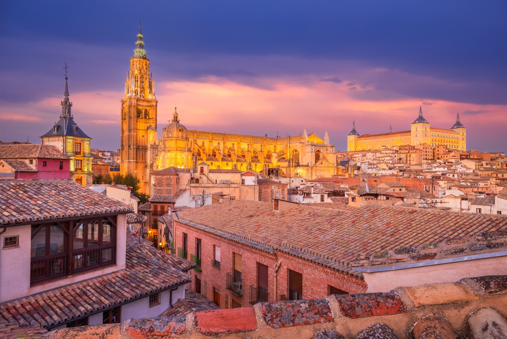 Dramatic aerial view of the medieval Toledo Cathedral and Alcazar fortress, twilight colored sky, Castilla La Mancha. The article is about things to buy from Amazon before going to Spain.
