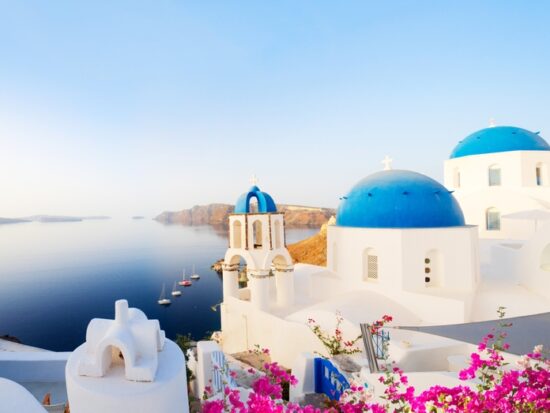 Traditional greek village Oia of Santorini, with blue domes against sea and caldera, Greece, web banner format. Article is about things to buy from Amazon for Greece.