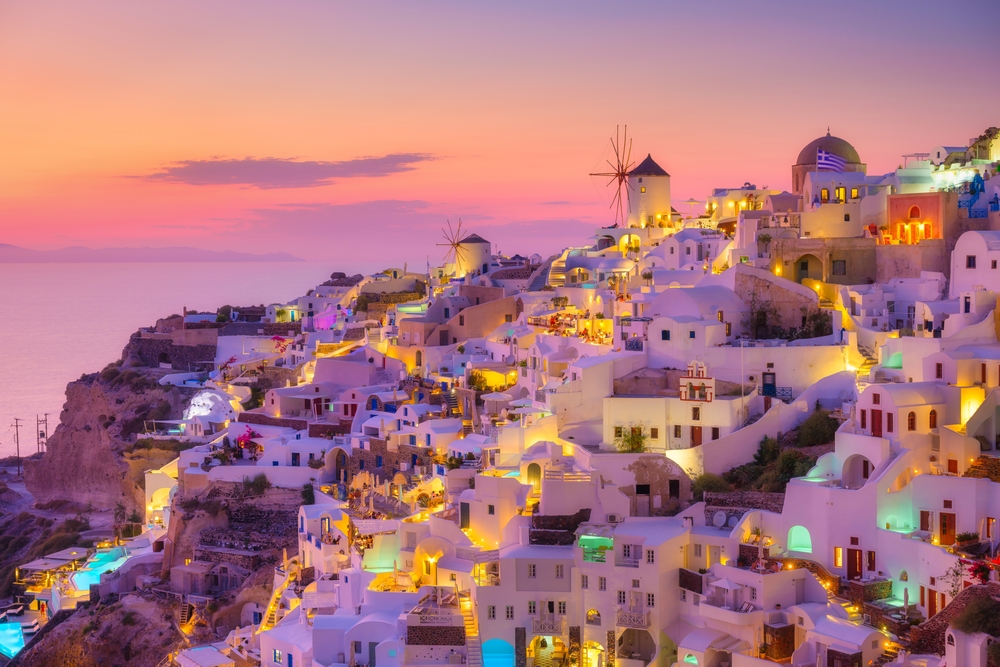 Oia village, Santorini, Greece. View of traditional houses in Santorini. Small narrow streets and rooftops of houses, churches and hotels. Landscape during sunset.