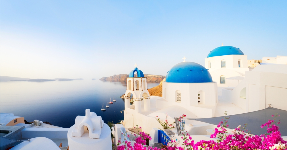 Traditional greek village Oia of Santorini, with blue domes against sea and caldera, Greece, web banner format. Article is about things to buy from Amazon for Greece.