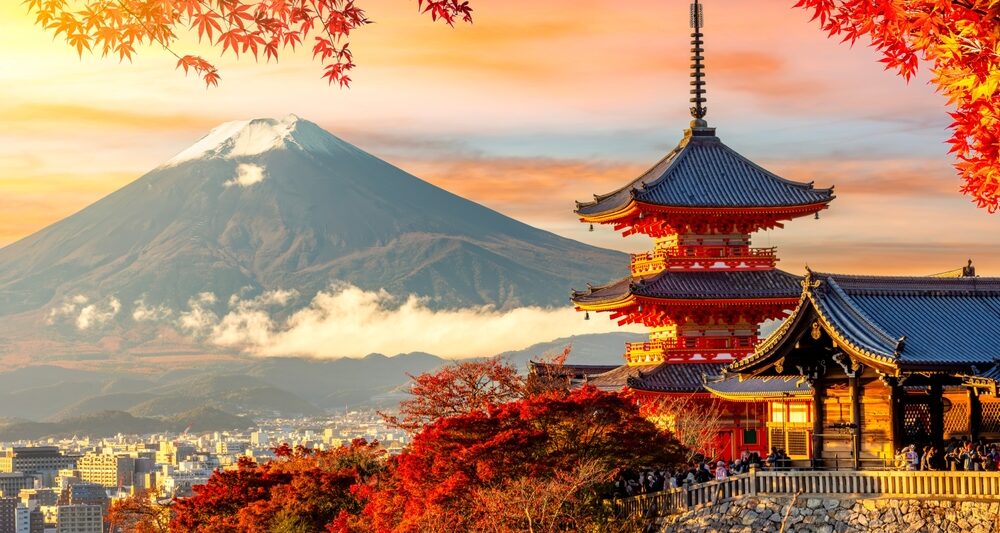 Kiyomizu-dera temple in Kyoto and mount Fuji at autumn sunset, Japan. it is sunset during the fall with fall foliage leaves framing the building with the mountain in the background. Article is about things to buy from Amazon for Japan.