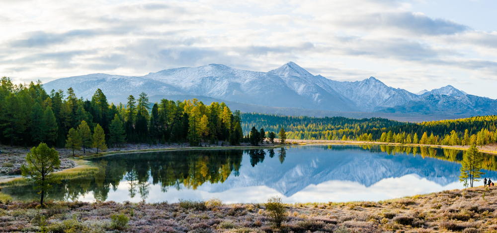 A lake with surrounding green trees and snow-capped mountains are in the background, and knowing where you are going helps you know what things to buy from amazon for vacation.