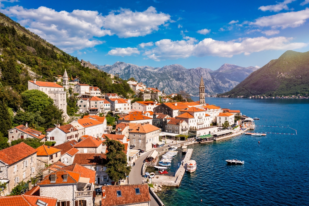 In Europe, a city with stone and white buildings and orange roofs sit on a road that leans against blue water, and knowing you're going somewhere like this helps you know what things to buy from amazon for vacation.