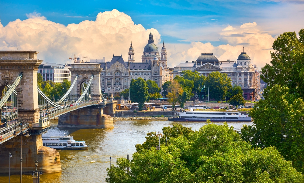 In a European city, boats travel on a river, under a boat, with towers and churches in the distance: knowing what things to buy from amazon for vacation helps prepare for cities like this.