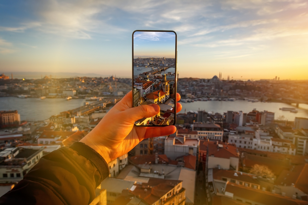 A hand holding a phone takes a photo of a city across a body of water at golden hour, and things like a phone charger are one of those things to buy from amazon for vacation that helped this photo happen.