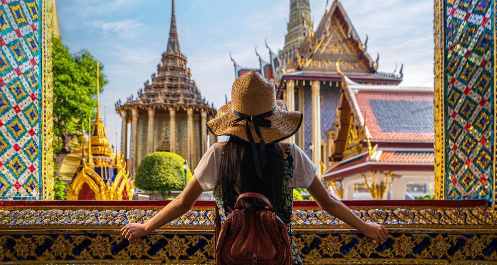 A woman overlooks the structure of colorful buildings in Asia, as she leans on an open window with ornate and colorful designs, full well knowing what things to buy from amazon for vacation and how they helped her for this trip.