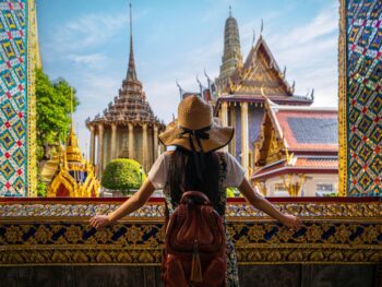 A woman overlooks the structure of colorful buildings in Asia, as she leans on an open window with ornate and colorful designs, full well knowing what things to buy from amazon for vacation and how they helped her for this trip.