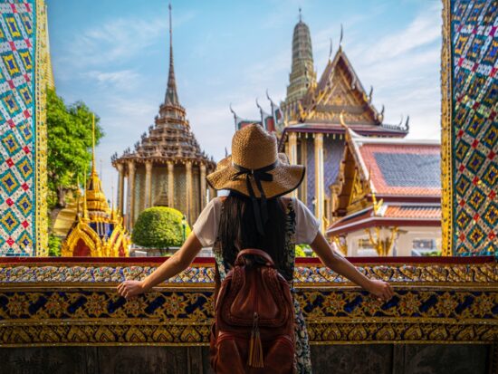 A woman overlooks the structure of colorful buildings in Asia, as she leans on an open window with ornate and colorful designs, full well knowing what things to buy from amazon for vacation and how they helped her for this trip.