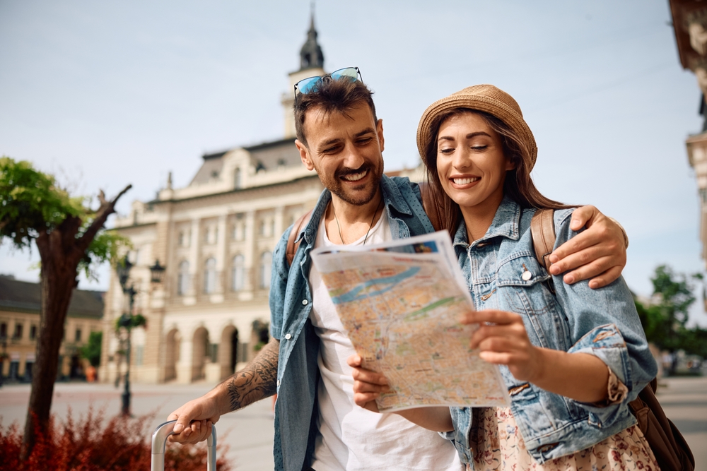 A man throws his arm around a woman as they navigate a map in an unfamiliar city.