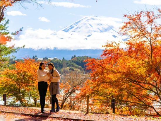 Two girls hover in the fall foliage of Japan, mountains in the background, and they are comfortable because they knew what to wear to Japan in the fall with their long pants, tights, midi skirts and sweaters.