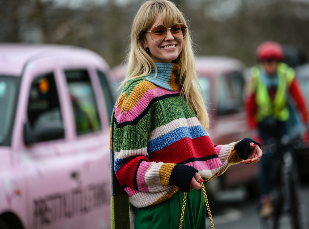 A young blonde in sunglasses stands in a street in London while wearing a turtle neck that is striped: she knows what to wear in London in September.