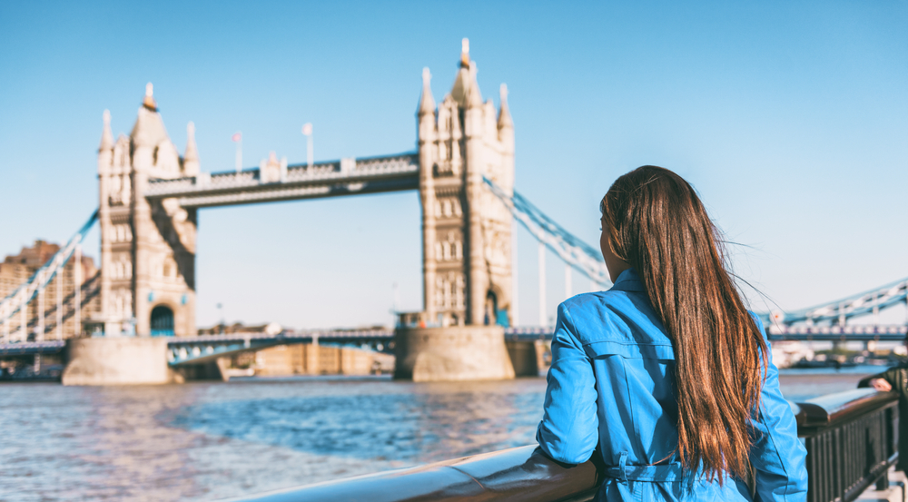 A girl in a blue jacket knows what to wear in London in September as she turns toward Tower Bridge and faces the chill of the wind off the water.
