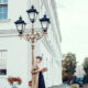 A woman leans against a lightpost in London, knowing what to wear in London in fall, in her pants , trench coat, and beret.