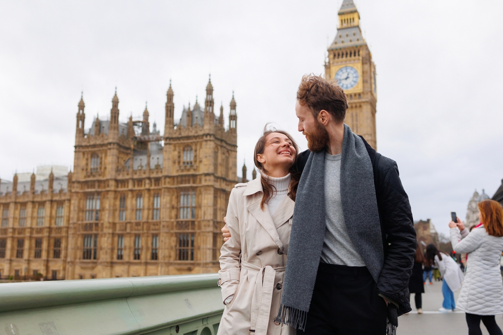 A couple walks down the bridge, leaving Parlament behind them as they wear wools shirts, scarfs and jackets, knowing what to wear in London in fall.