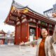 A woman in a plaid wool jacket over a turtleneck knows what to wear in Tokyo as she takes a selfie during the fall season at a famous temple in Japan.