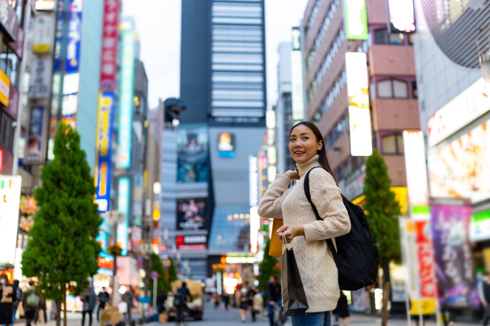 A woman knows what to wear in Tokyo in the fall as she stands in the middle of the city hub street wearing a knit sweater dress that doubles as a turtleneck for extra warmth.