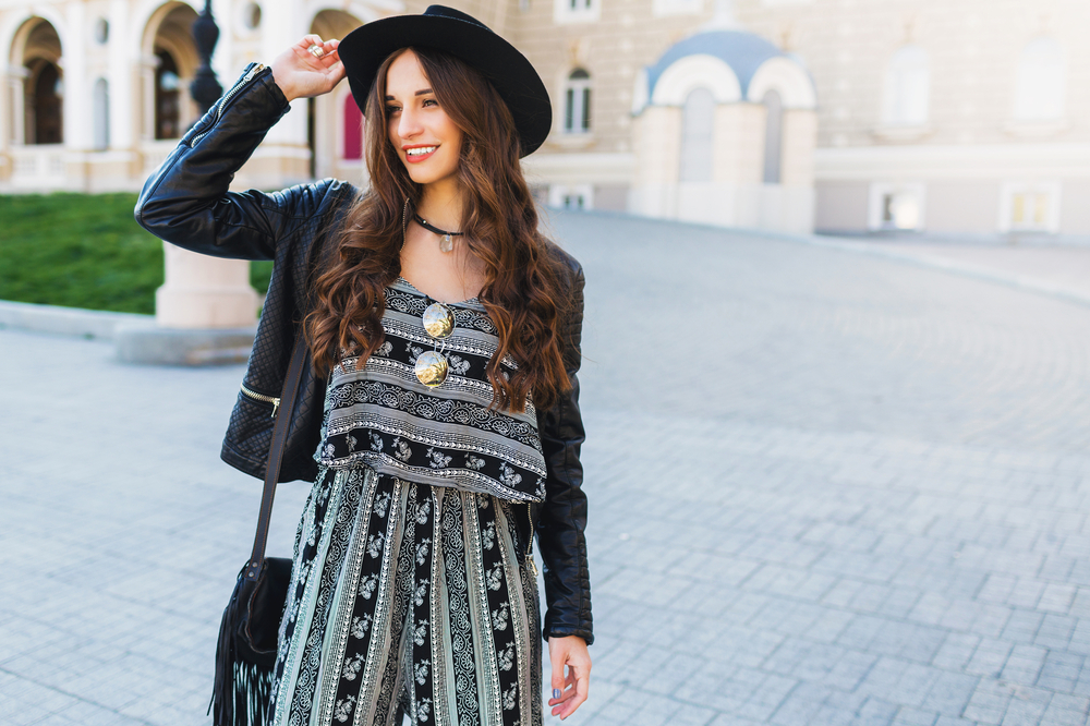 A young girl in a patterned Maxi dress, leather jacket and hat smiles in the streets of Paris.