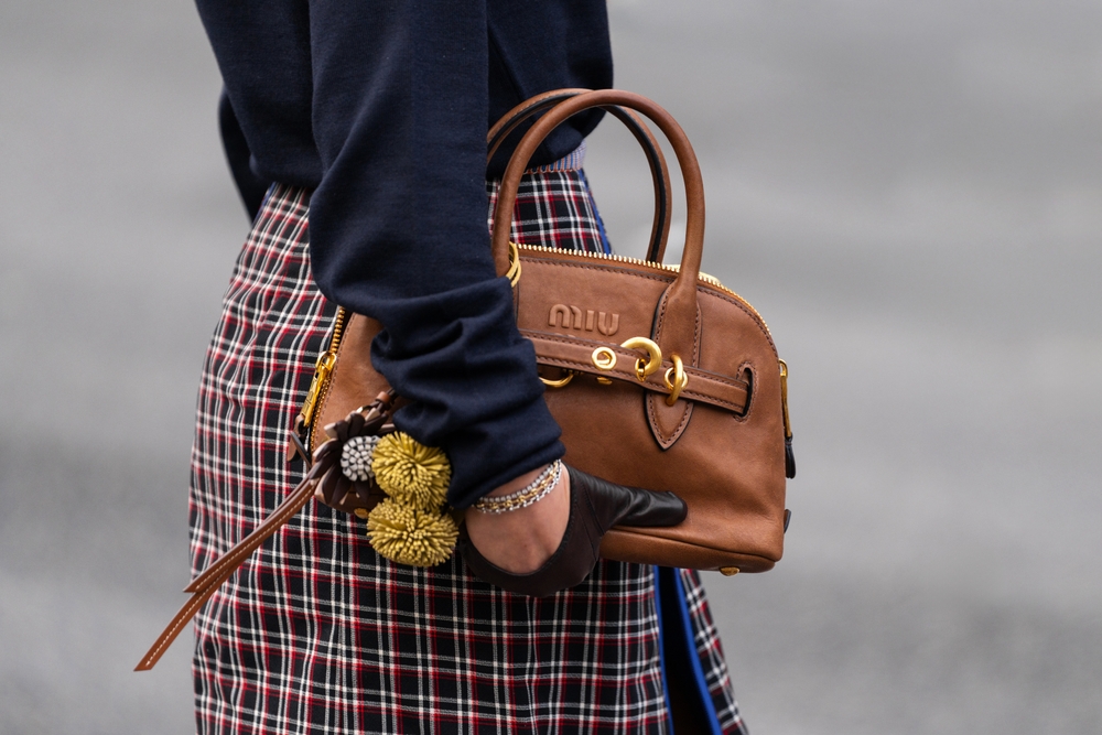 A woman carries a beige purse with her gloved hand and her plaid skirt, knowing what to wear to Paris in September.