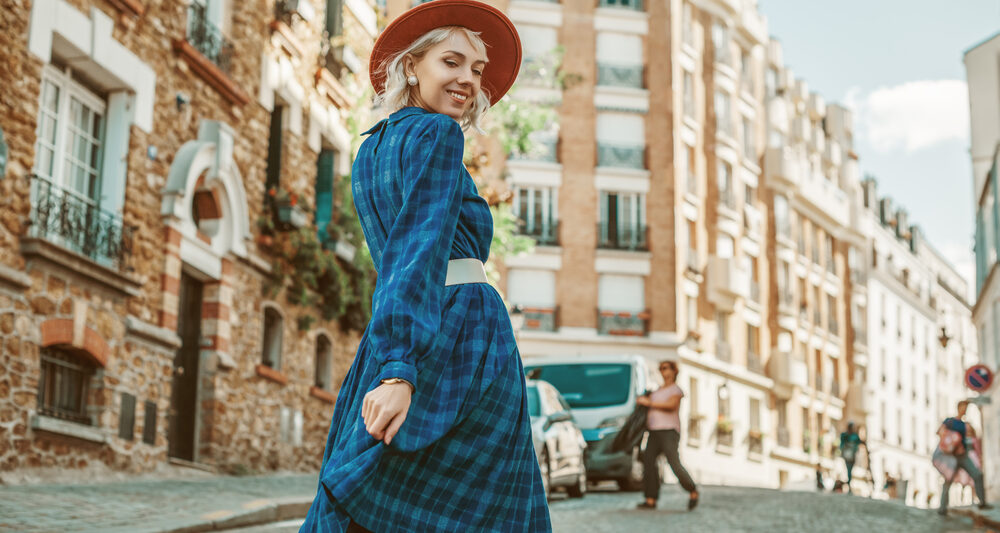 A woman in a plaid skirt and red beret walks down the streets of Paris, looking over her shoulder, knowing what to wear to Paris in September.