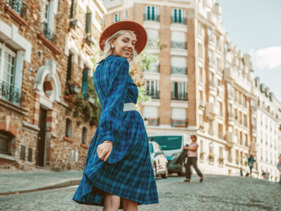 A woman in a plaid skirt and red beret walks down the streets of Paris, looking over her shoulder, knowing what to wear to Paris in September.