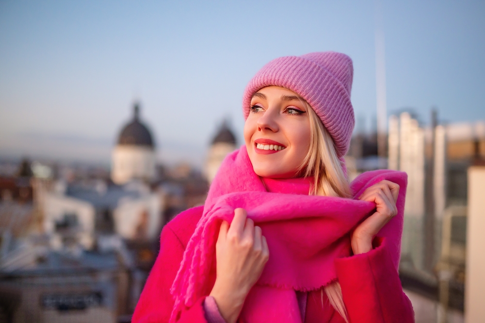 Woman wearing trendy total pink outfit with knitted beanie hat, woolen scarf, coat, posing outdoor.