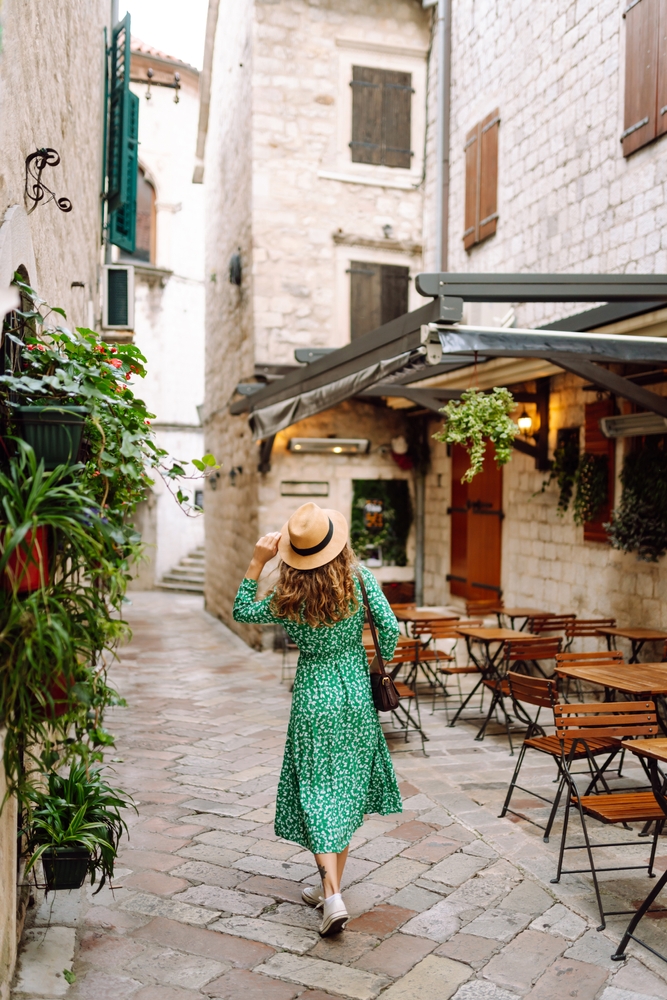woman with curly hair strolling through a picturesque town square adorned with architecture and outdoor cafés. European city.