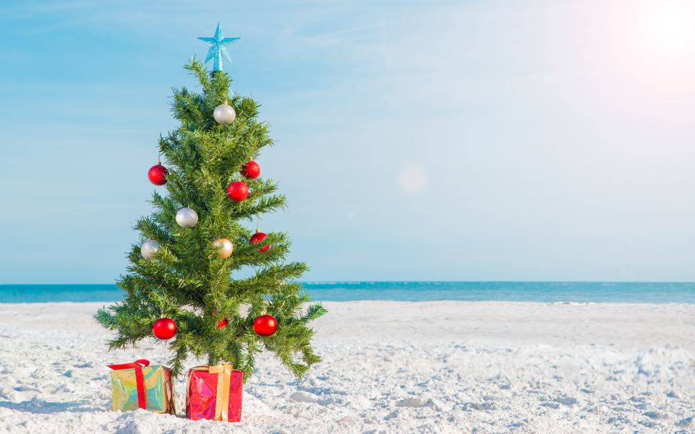 A Christmas tree with a star and red and silver ornaments sits on the beach, because there are a ton of Best Places to Celebrate Christmas on The Beach!