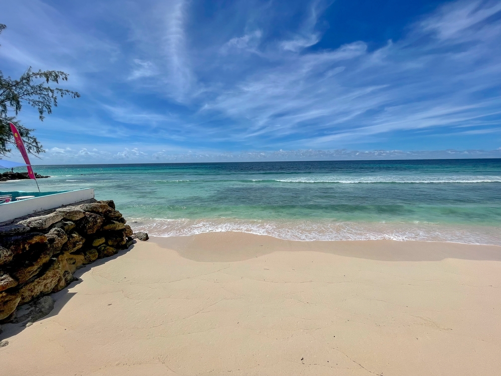 A photo of Barbados shows blue waters breaking in waves on the calm shore.