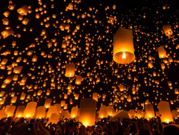 Chiang Mai festival in Thailand, a traditional festival, Yi Peng Lantern. You can see lots of lanterns in the dark sky. the lanterns are glowing with a candle underneath of them and they are orange against the black night sky