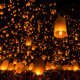 Chiang Mai festival in Thailand, a traditional festival, Yi Peng Lantern. You can see lots of lanterns in the dark sky. the lanterns are glowing with a candle underneath of them and they are orange against the black night sky