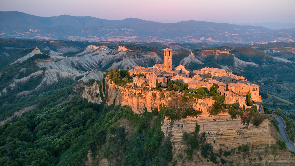 Civita di Bagnoregio, aerial view of ancient Italian city standing on top of a plateau, illuminated by setting sun. The article is about fairytale destinations.