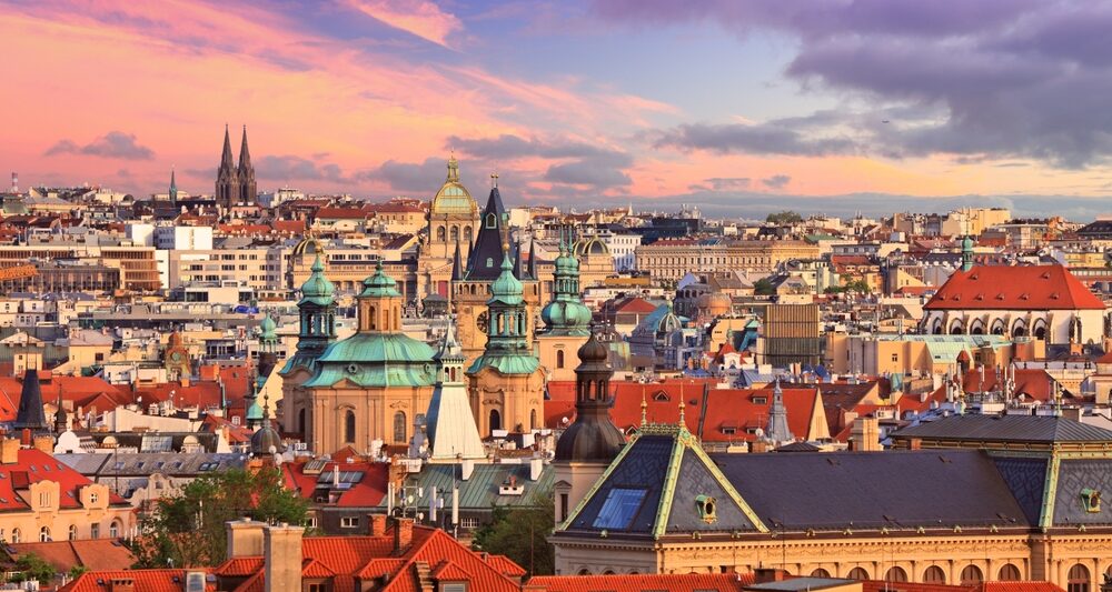photo of sprawling prague cityscape at sunset, spires are reaching up over smaller buildings