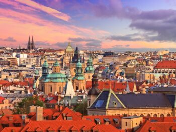 photo of sprawling prague cityscape at sunset, spires are reaching up over smaller buildings