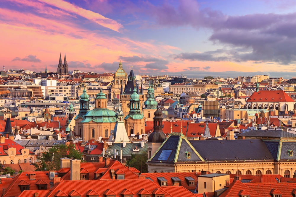 photo of sprawling prague cityscape at sunset, spires are reaching up over smaller buildings