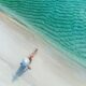 Woman from above wearing a white hat on the background of the sea and sunny beach. The article is about things to buy from Amazon before your beach vacation.