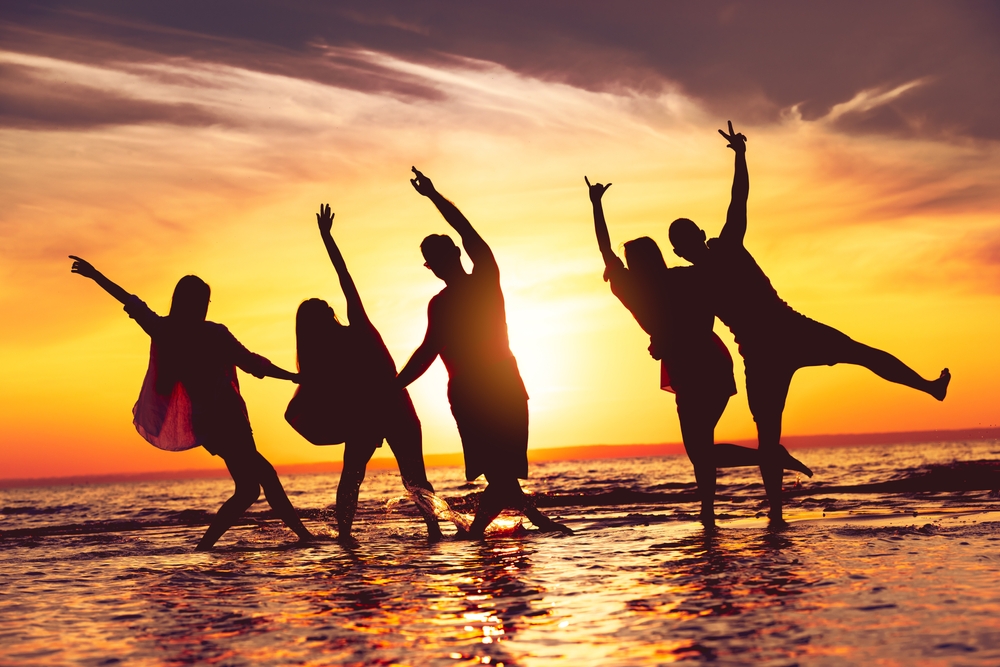 Group of happy friends are having fun at sunset beach. The article is about things to buy from Amazon before your beach vacation.