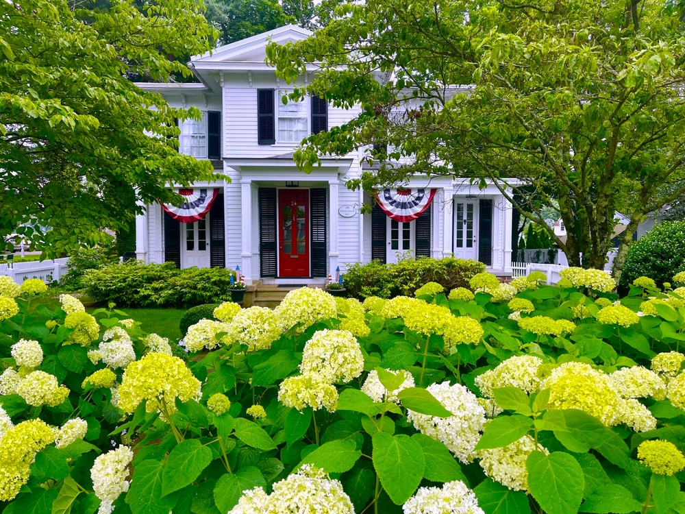 A house in Essex Connecticut is adorned with blooming flowers in it's front yard.