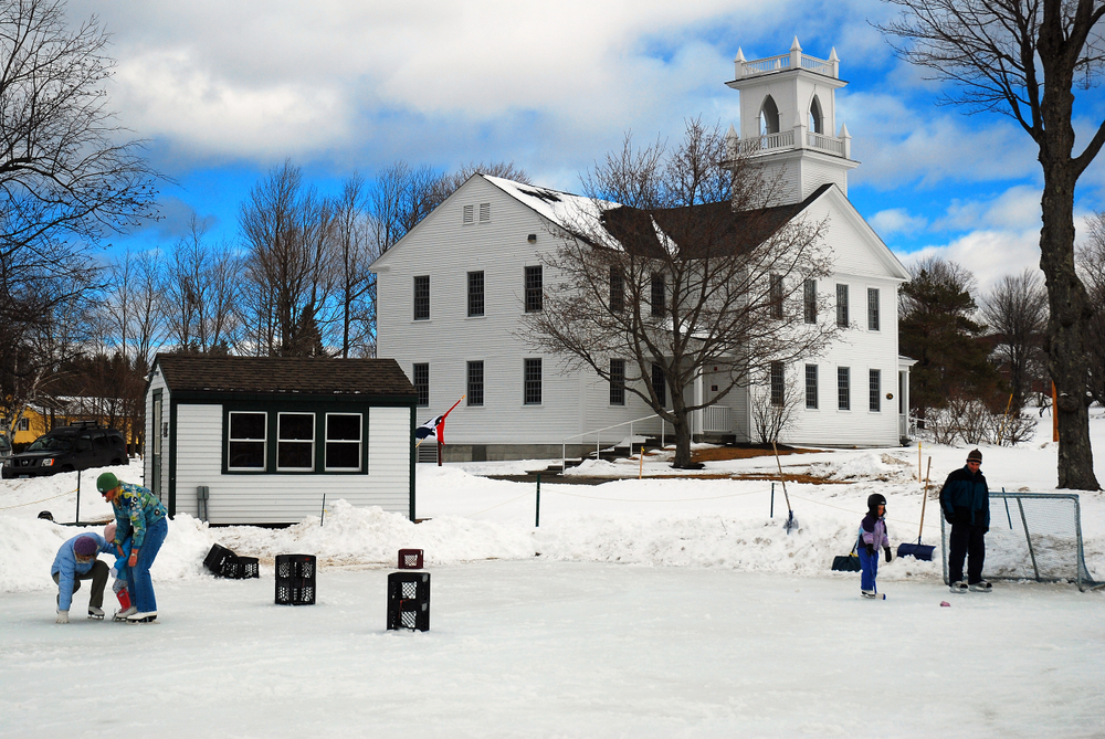 People gather on a frozen pond to ice skate and play hockey in New London, New Hampshire. The article is about towns in New England that feel like a hallmark movie.