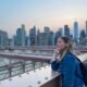 A woman overlooks the water on the Brooklyn bridge with a backpack on while wearing a denim jacket: she is well prepared to enjoy the city as she knew what to wear in New York City in September.