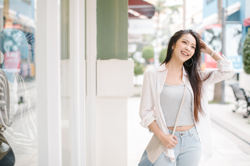 A woman smiles as she runs her hand through her hair during a warmer day in fall: she knew what to wear in New York City in September in her light blouse and jeans.