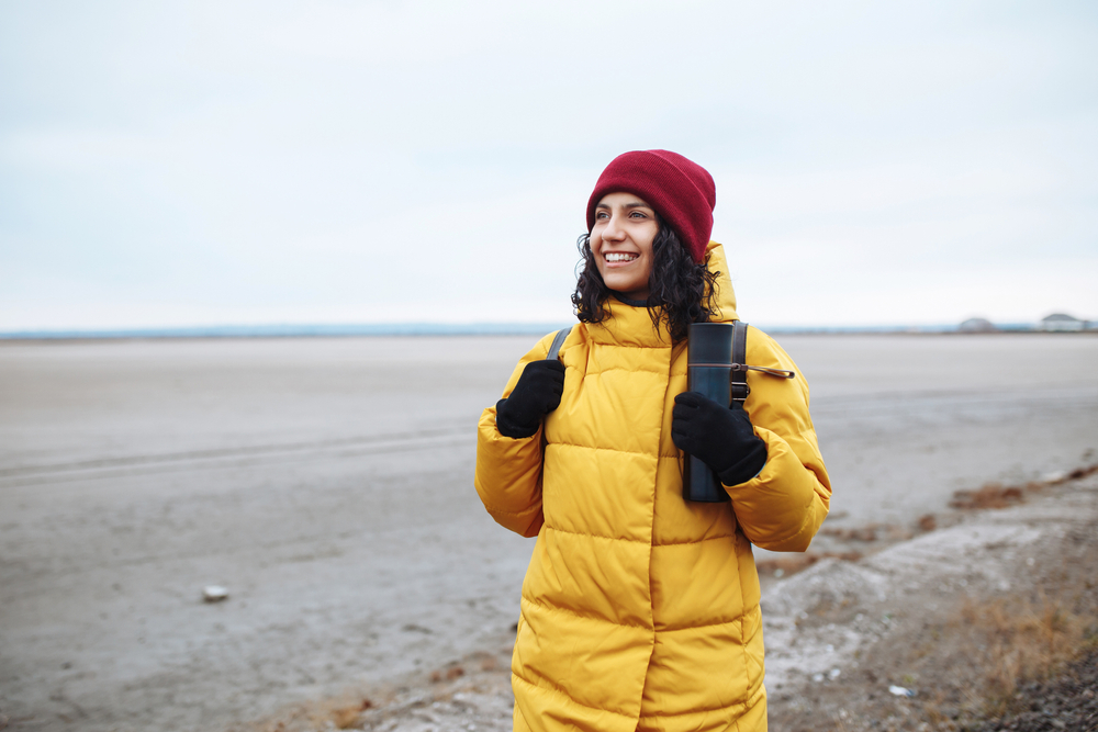 A woman in a yellow parka, gloves, and red beanie smiles as she explores Iceland.